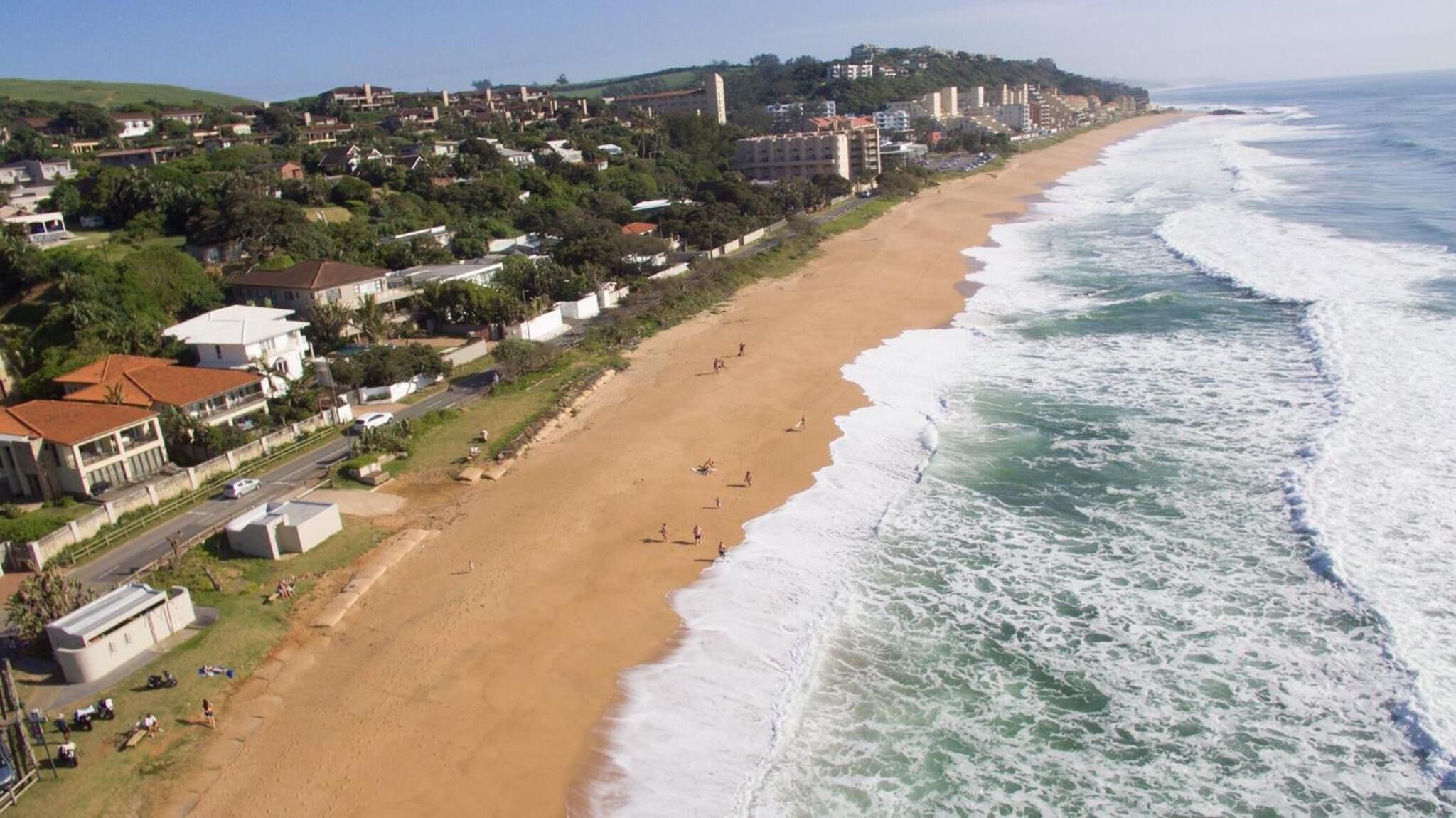 Una playa costera con casas a lo largo de la orilla y una carretera paralela a la playa.