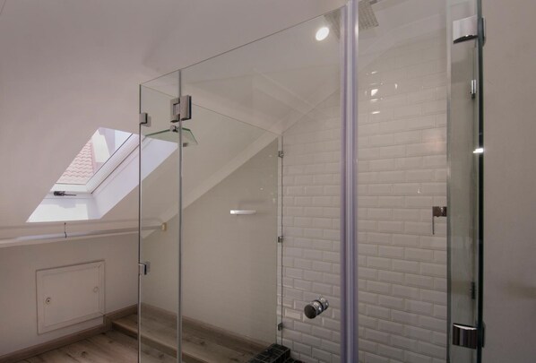Un baño moderno con cabina de ducha de vidrio, paredes de azulejos blancos y tragaluz.