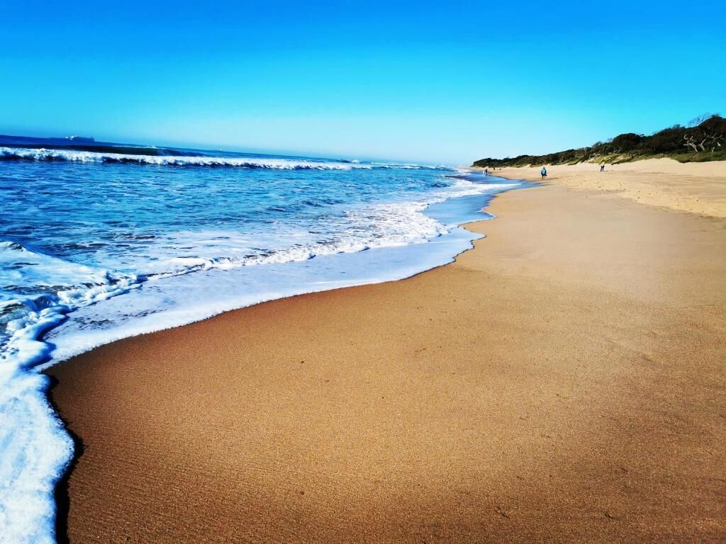 A beach with a clear sky, waves, and a sandy shore.