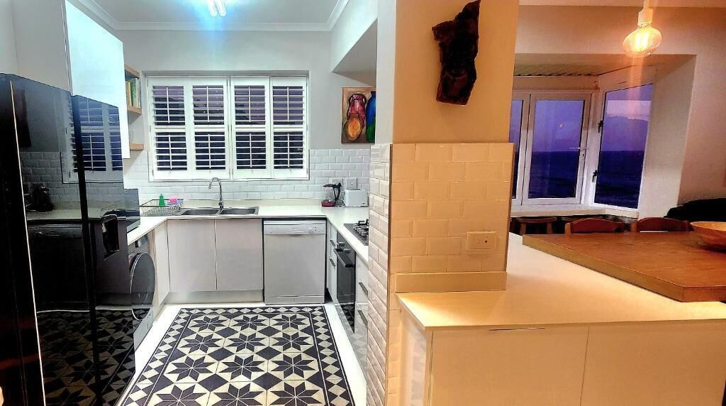 A compact kitchen with a window, a tiled floor, and a dining area with a view.