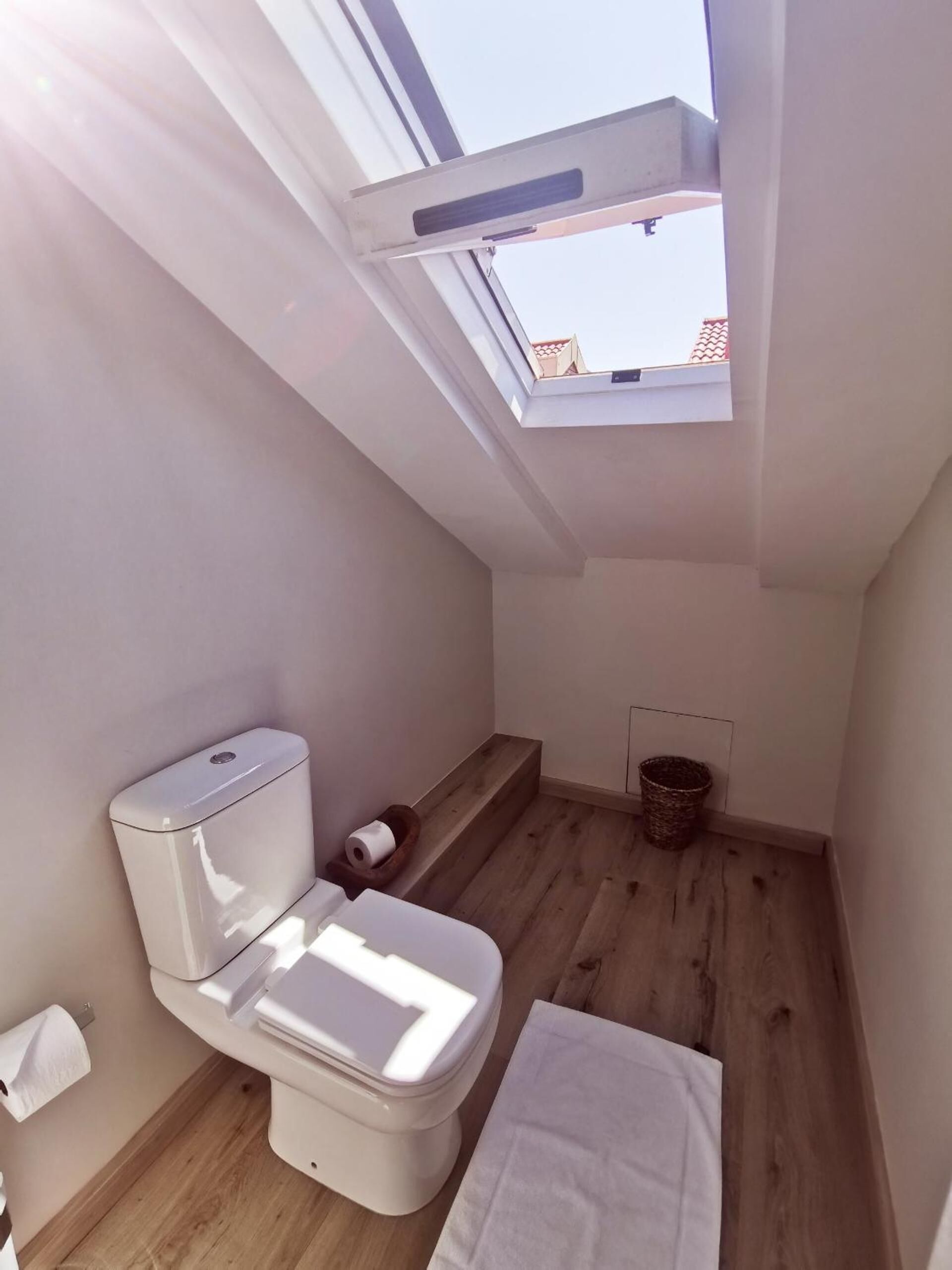Ein kleines, helles Badezimmer mit Oberlicht, Toilette, Holzboden und einem weißen Handtuch auf dem Boden.