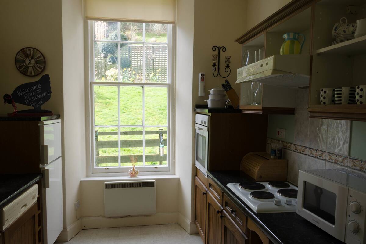 A kitchen with a large window, a stove, a microwave, and various kitchen utensils.