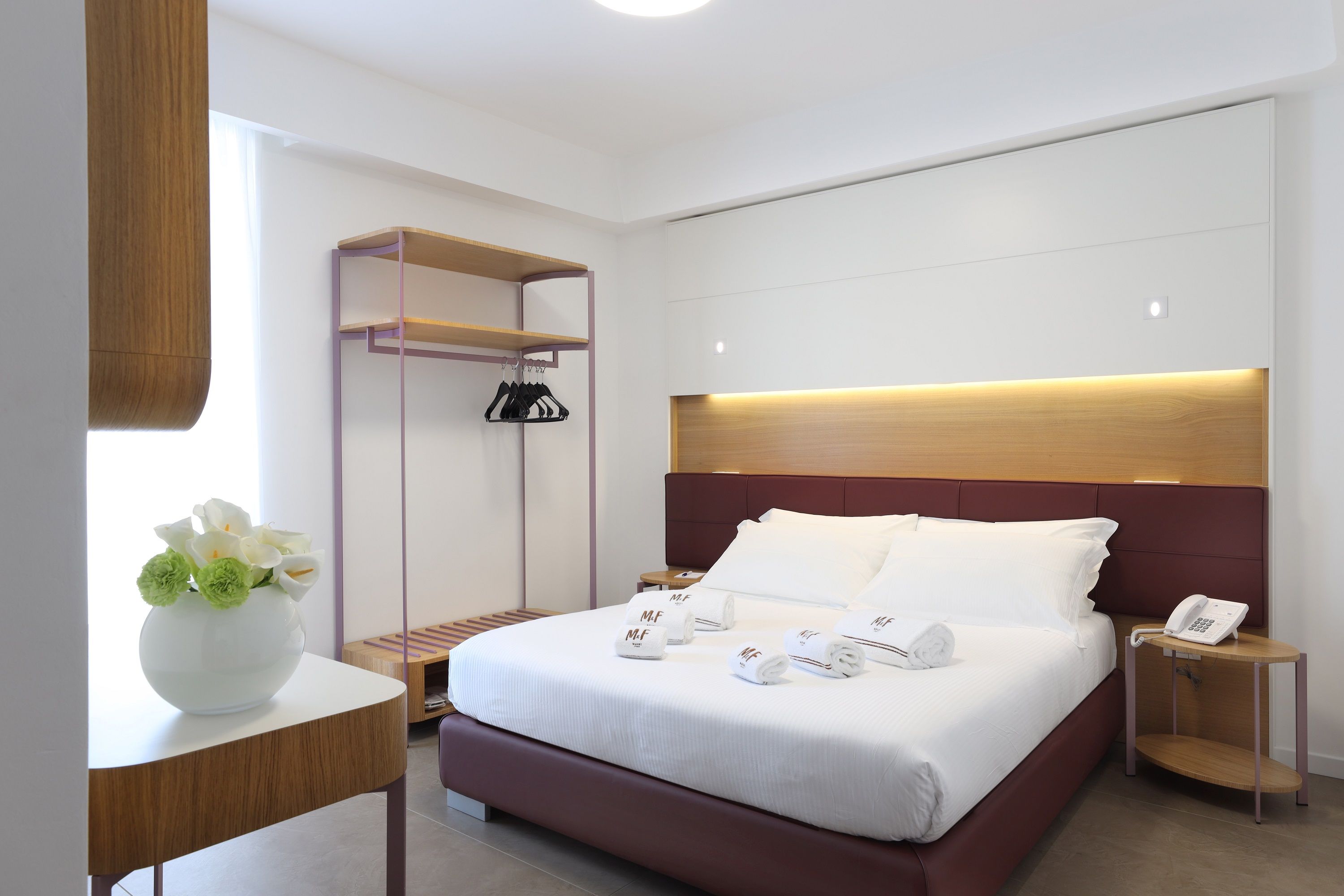Une chambre d’hôtel moderne avec un grand lit, des tables de chevet, une armoire et une petite table sur laquelle est posé un vase de fleurs.