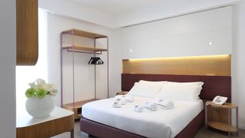 A modern hotel room with a large bed, bedside tables, a wardrobe, and a small table with a vase of flowers.