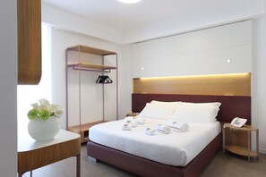 A modern hotel room with a large bed, bedside tables, a wardrobe, and a small table with a vase of flowers.