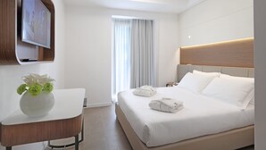 Habitación de hotel moderna con una cama grande, un televisor de pantalla plana en la pared, una mesita con un jarrón de flores y una ventana con cortinas.