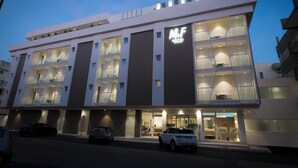 Un hotel moderno con un llamativo letrero 'M.F', ventanas grandes y una entrada bien iluminada.
