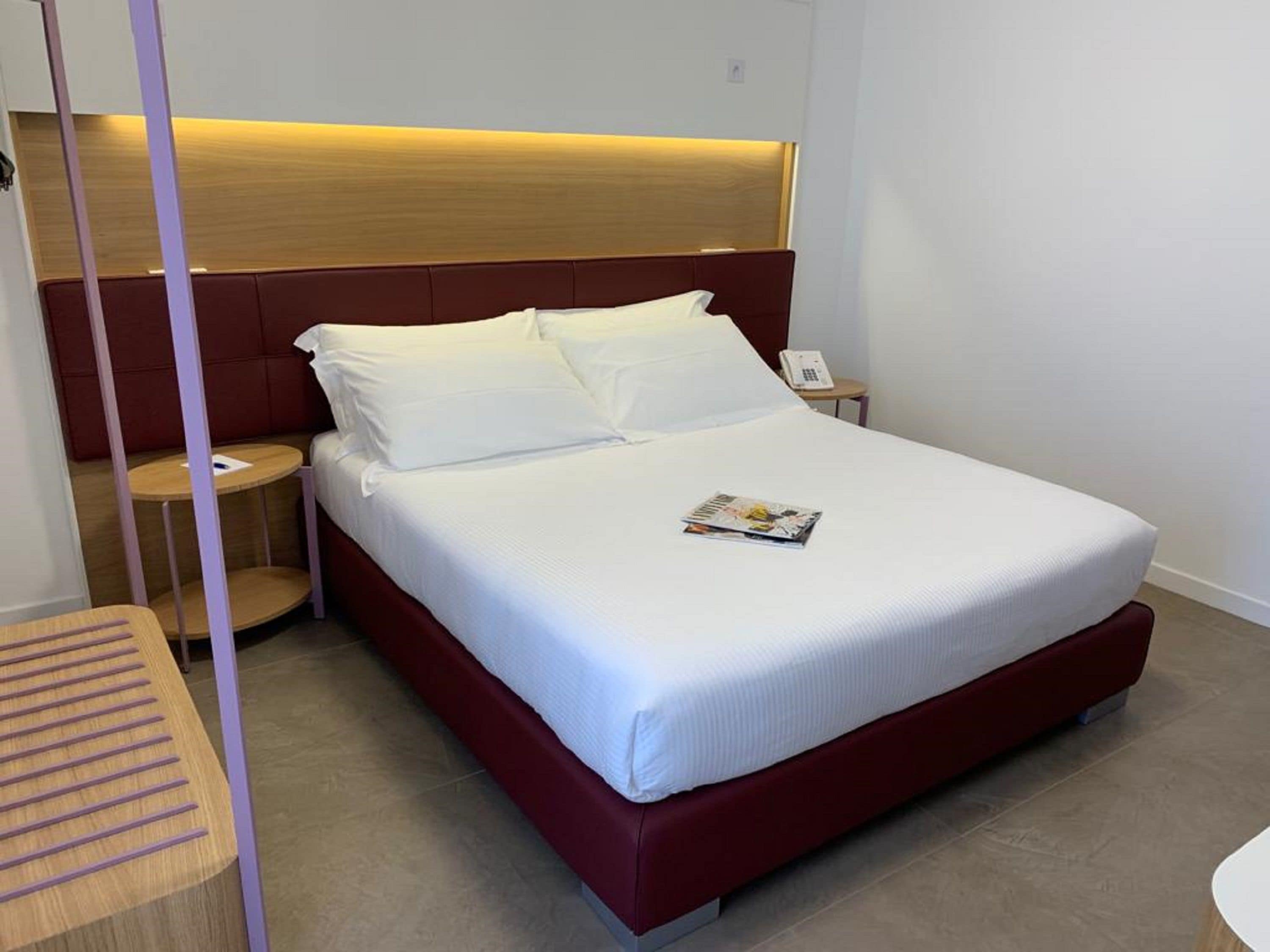 A neatly made bed with white linens, a wooden headboard, and a bedside table with a phone.