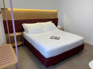 A neatly made bed with white linens, a wooden headboard, and a bedside table with a phone. - M&F Hotel (Gallipoli)