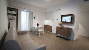 A modern living room with a sofa, a dining table with chairs, a kitchen area with cabinets, and a TV mounted on the wall. - M&F Hotel (Gallipoli)