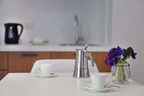 A white table with two white cups, a black coffee pot, and a clear glass vase with purple flowers. - M&F Hotel (Gallipoli)