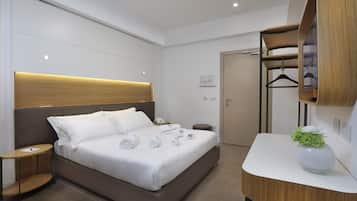 A modern hotel room with a large bed, bedside tables, a wooden headboard, a mirror, and a small plant on a bedside table.