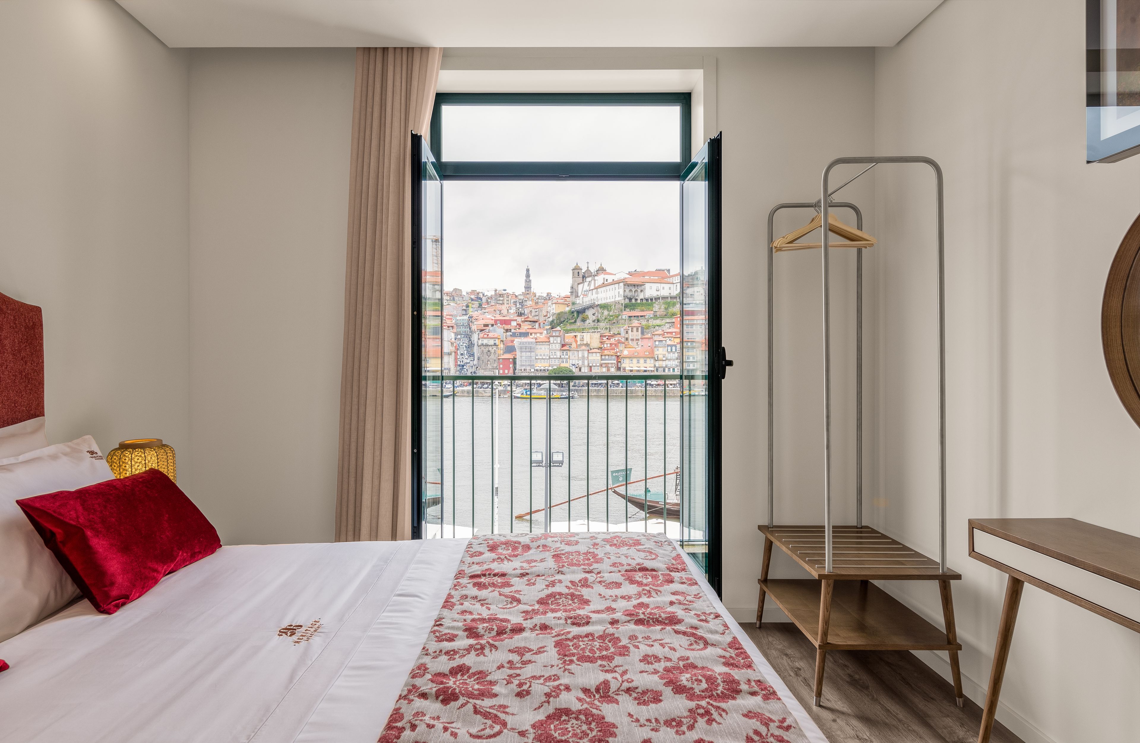 A hotel room with a bed, a hanging clothes rack, and a view of a cityscape through a window.