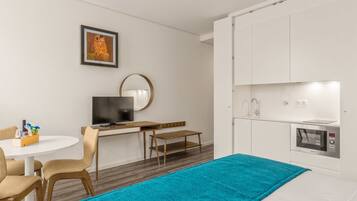 Habitación de hotel moderna con zona de comedor, televisor, cocina equipada con microondas y un gran ventanal.