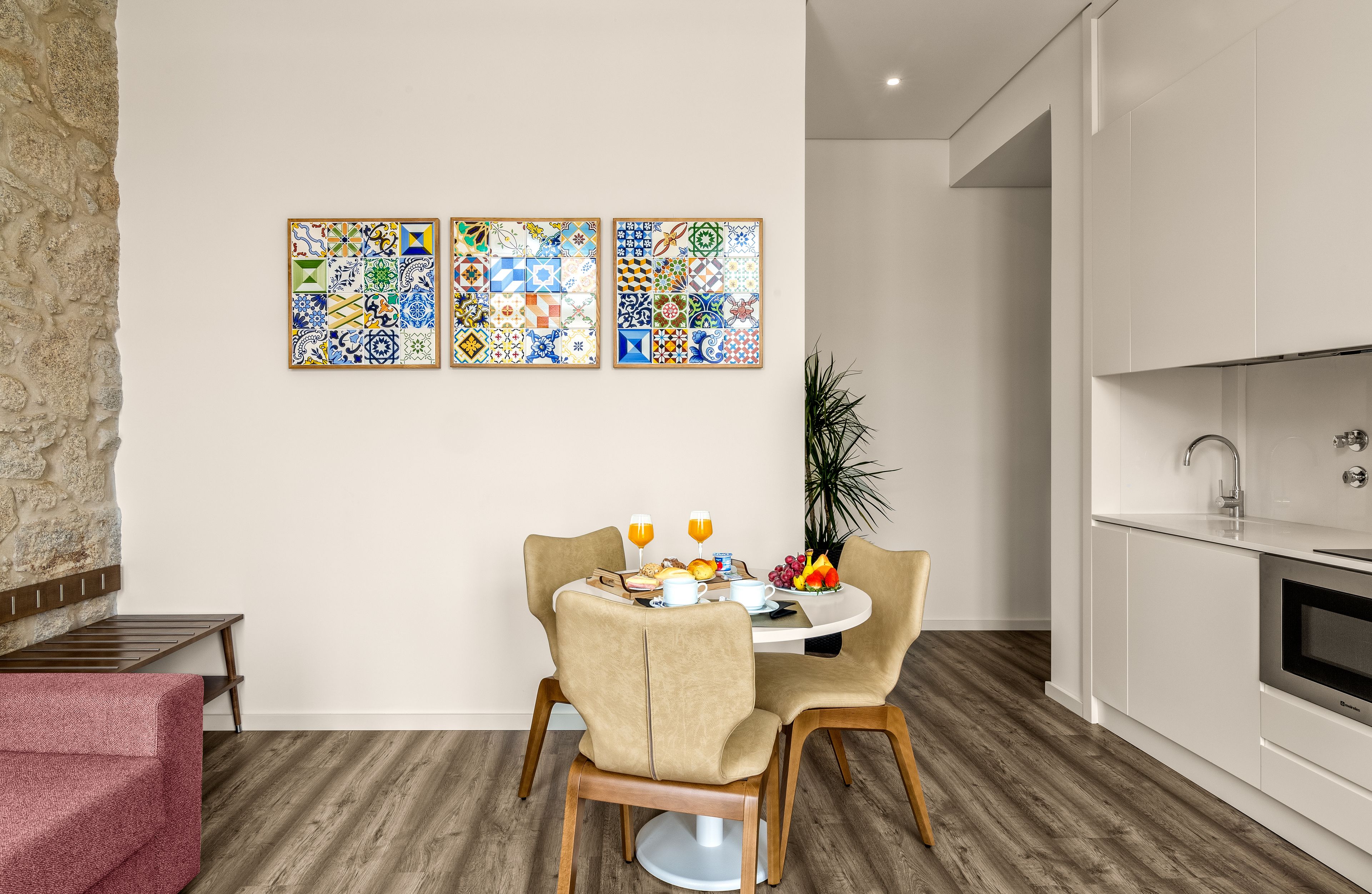 Een moderne keuken met witte kasten, een eethoek met een ronde tafel en stoelen, en een wand met drie ingelijste tegeltableaus.