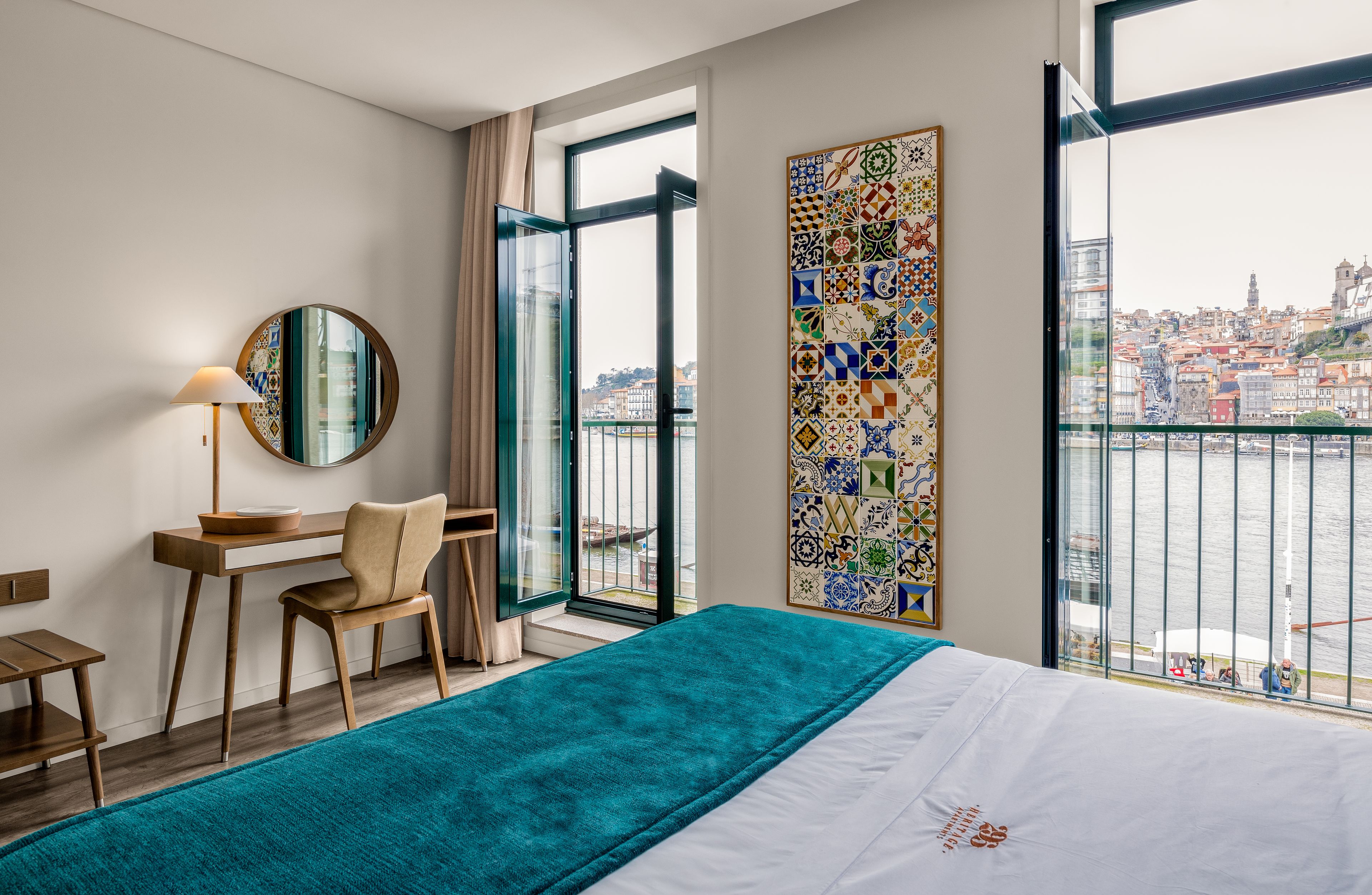 Ein Hotelzimmer mit Bett, Schreibtisch, Stuhl, großem Fenster und einer Wand mit dekorativen Fliesen. Blick auf die Stadt.