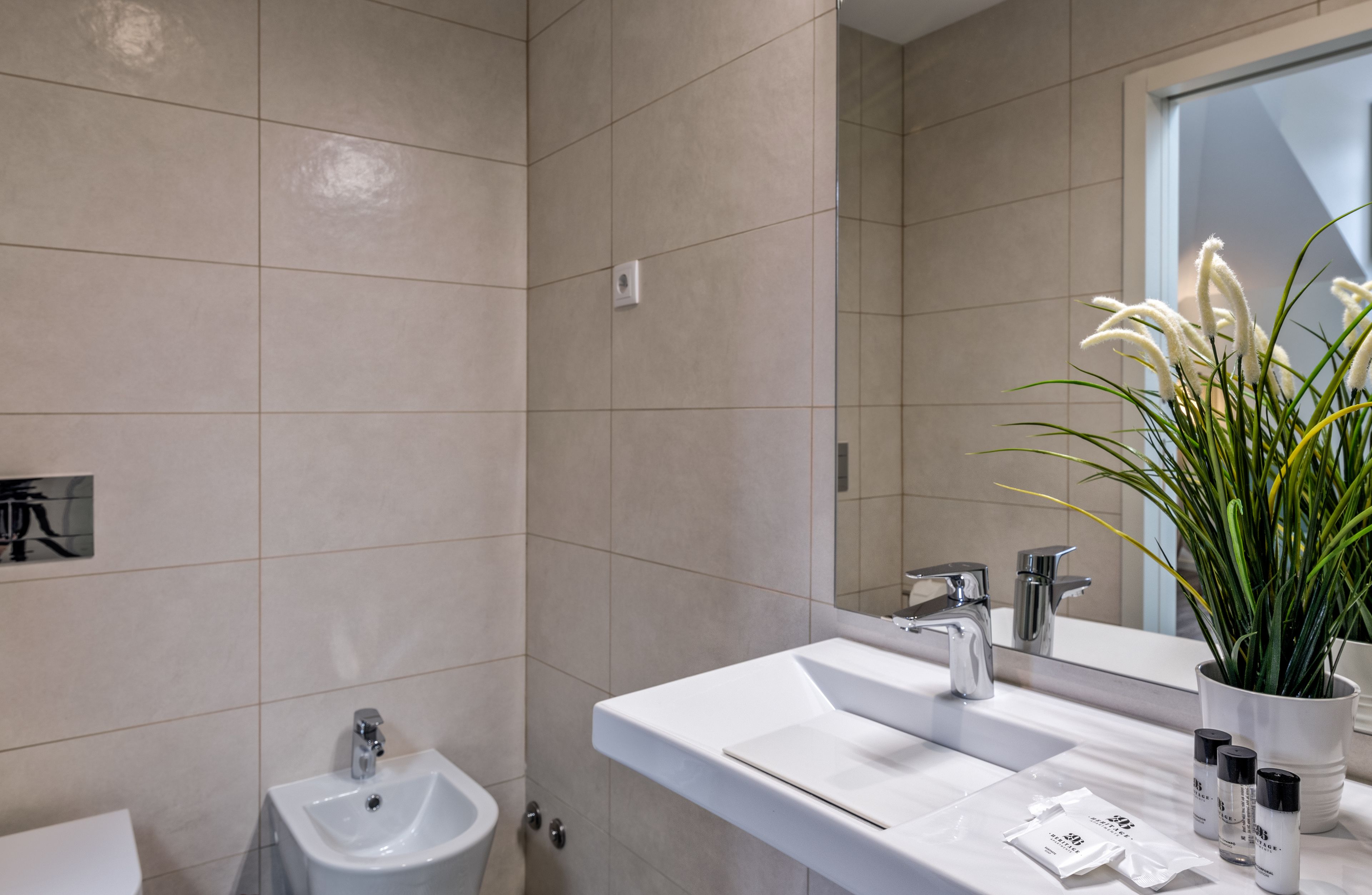 A modern bathroom with a white sink, mirror, and a potted plant.