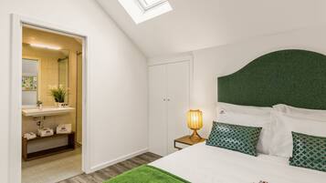 Un dormitorio con tragaluces, una cama con almohadas verdes, una lámpara de noche y vistas al baño.