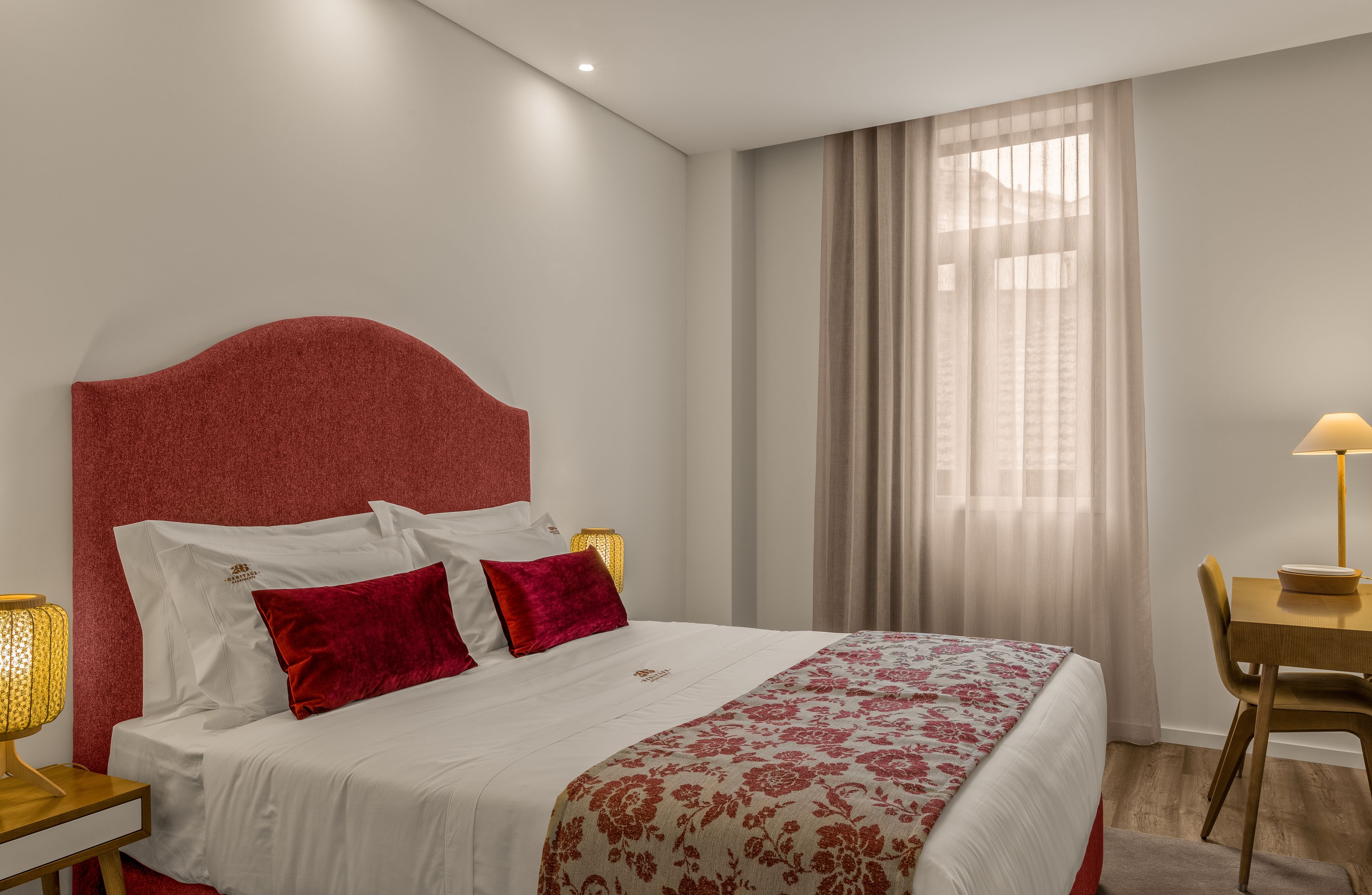 A hotel room with a bed, a desk, and a window with curtains.