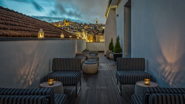A rooftop terrace with striped sofas and round tables, overlooking a cityscape at dusk. - 296 Heritage Apartments (Vila Nova de Gaia)