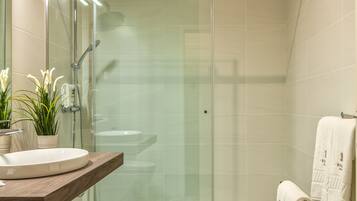 Un baño moderno con cabina de ducha de vidrio, tocador de madera con lavamanos y baldosas de suelo estampadas.