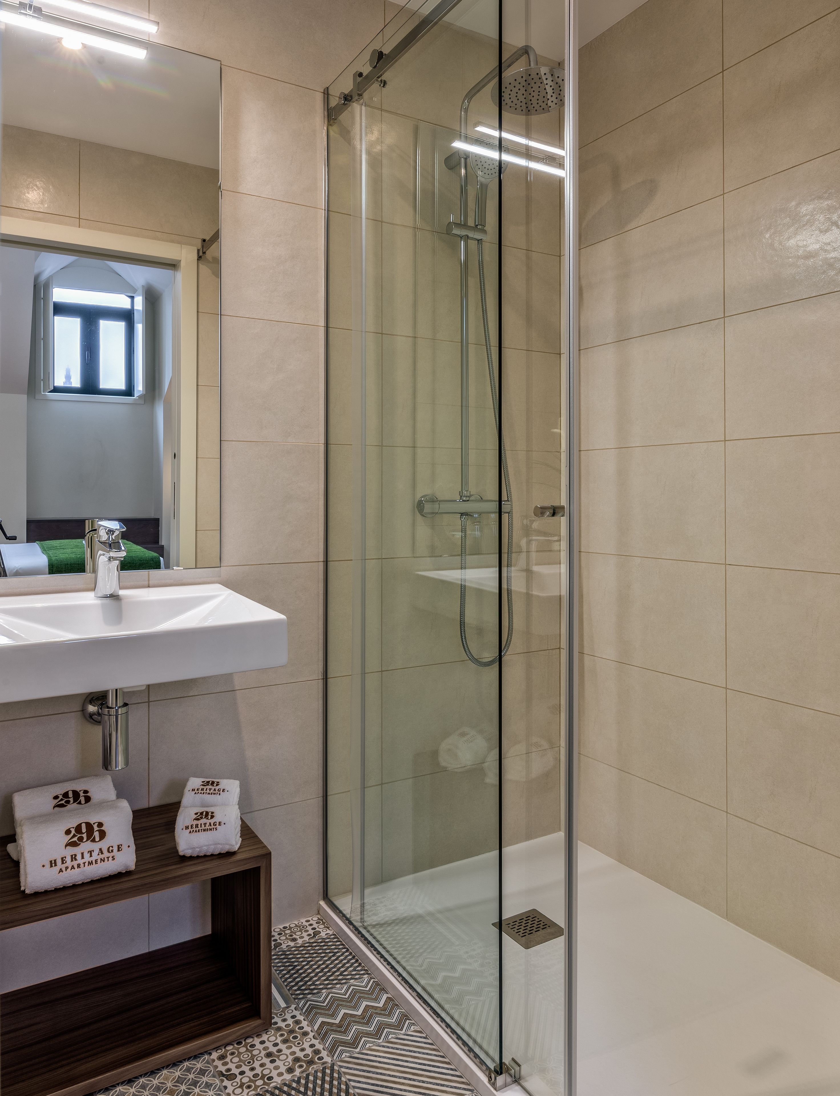 A modern bathroom with a glass-enclosed shower, a white sink, and a small shelf with towels.