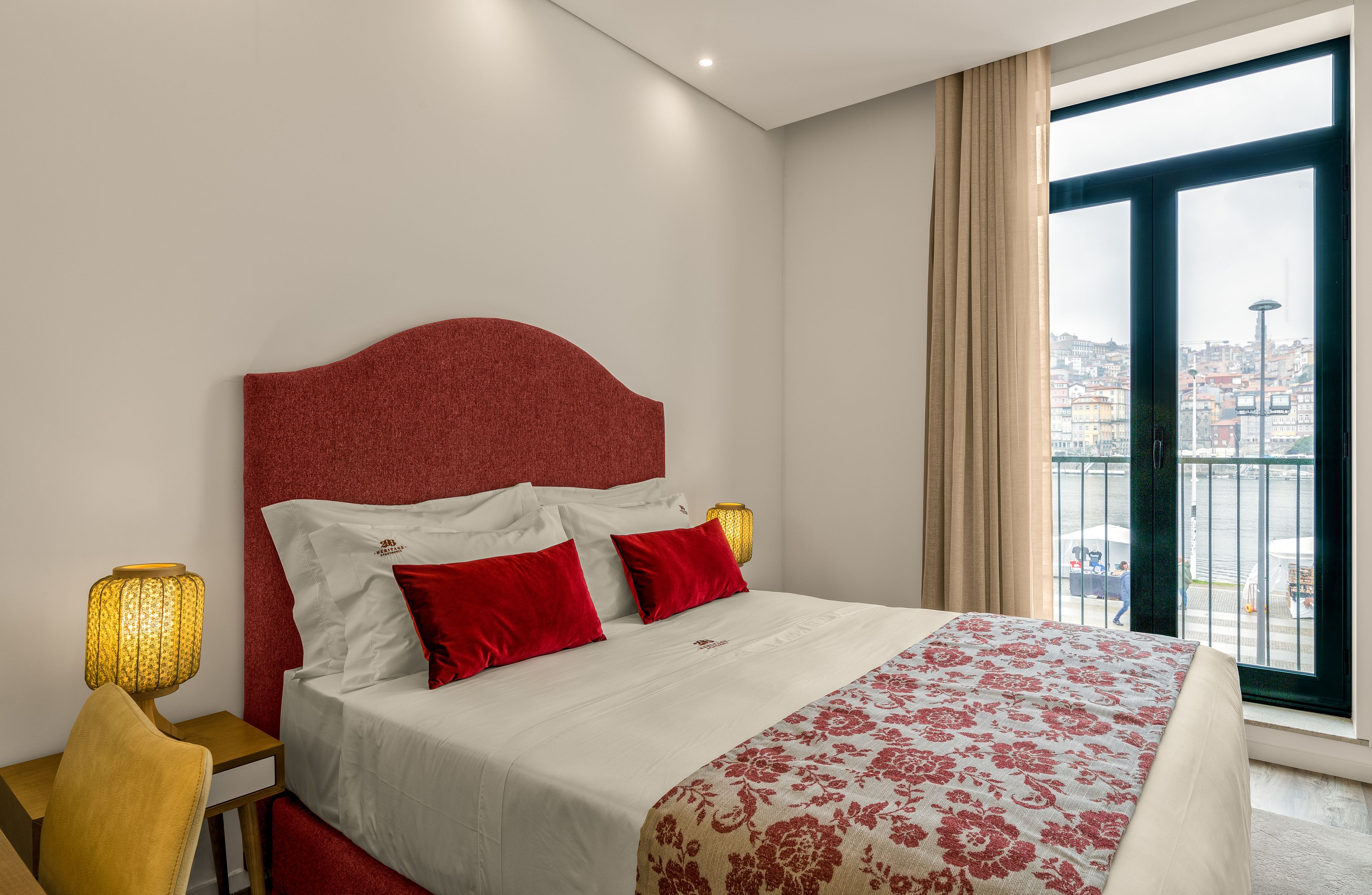 A hotel room with a bed, a view of the city, and a window with curtains.