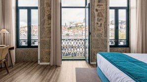 A hotel room with a large bed, a desk, and a view of a cityscape through large windows. - 296 Heritage Apartments (Vila Nova de Gaia)