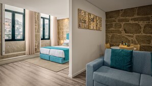 A modern bedroom with a large window, a bed, a sofa, and a stone wall with artwork. - 296 Heritage Apartments (Vila Nova de Gaia)