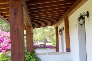 Un porche cubierto con vigas de madera y una pared blanca con una ventana.