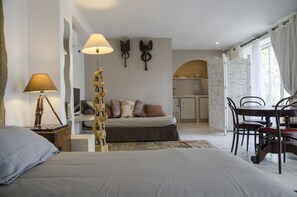 Un dormitorio con cama, lámpara de noche y una mesita con lámpara. Hay un comedor con una mesa y sillas.
