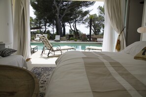 Un dormitorio con una cama grande, vista a una piscina y mobiliario exterior.