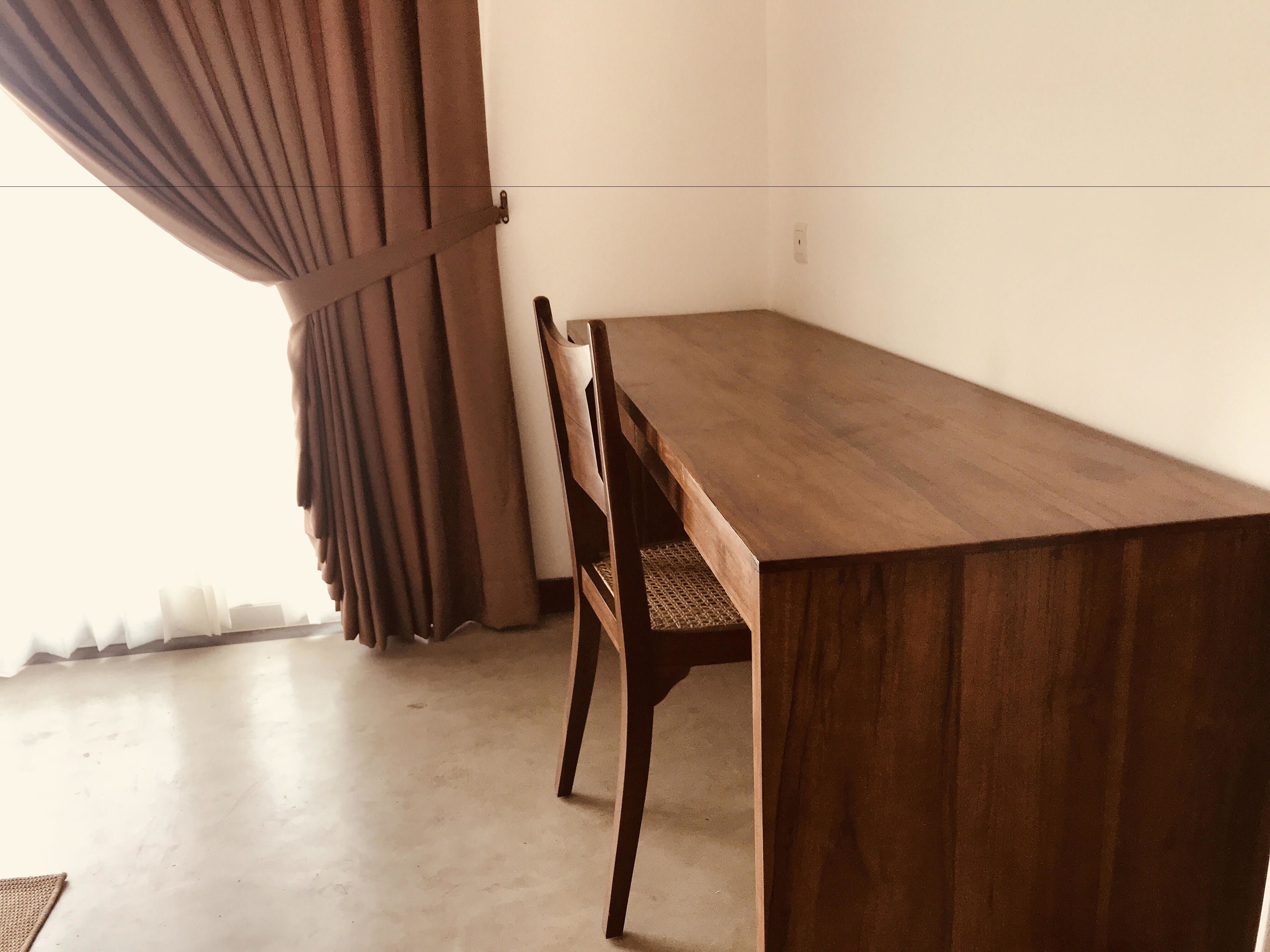 Una mesa de madera con sillas, una cortina y una pared sencilla.