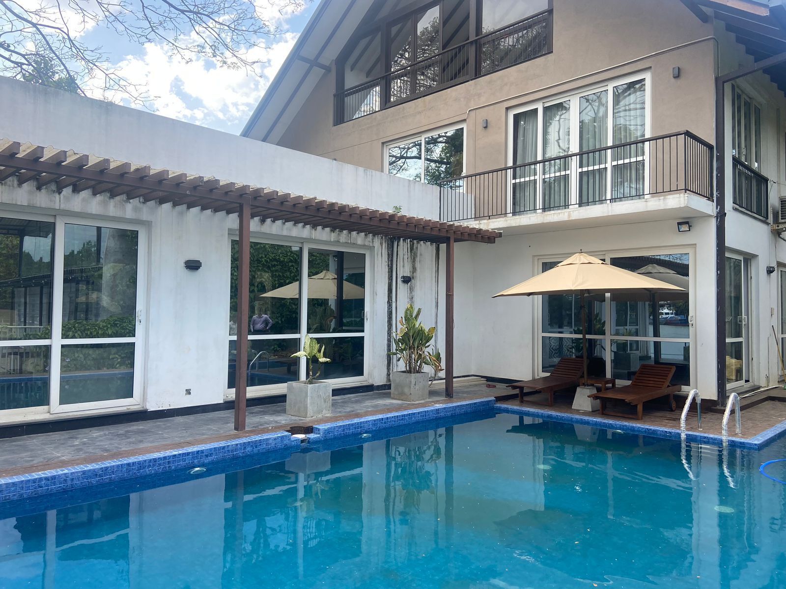 Une maison moderne à deux étages, dotée d’une piscine, de grandes fenêtres et d’un espace salon extérieur.