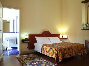 A bedroom with a bed, a nightstand, a lamp, a mirror, and a bathroom visible through an open door. - Le Muse B&B (Locri)