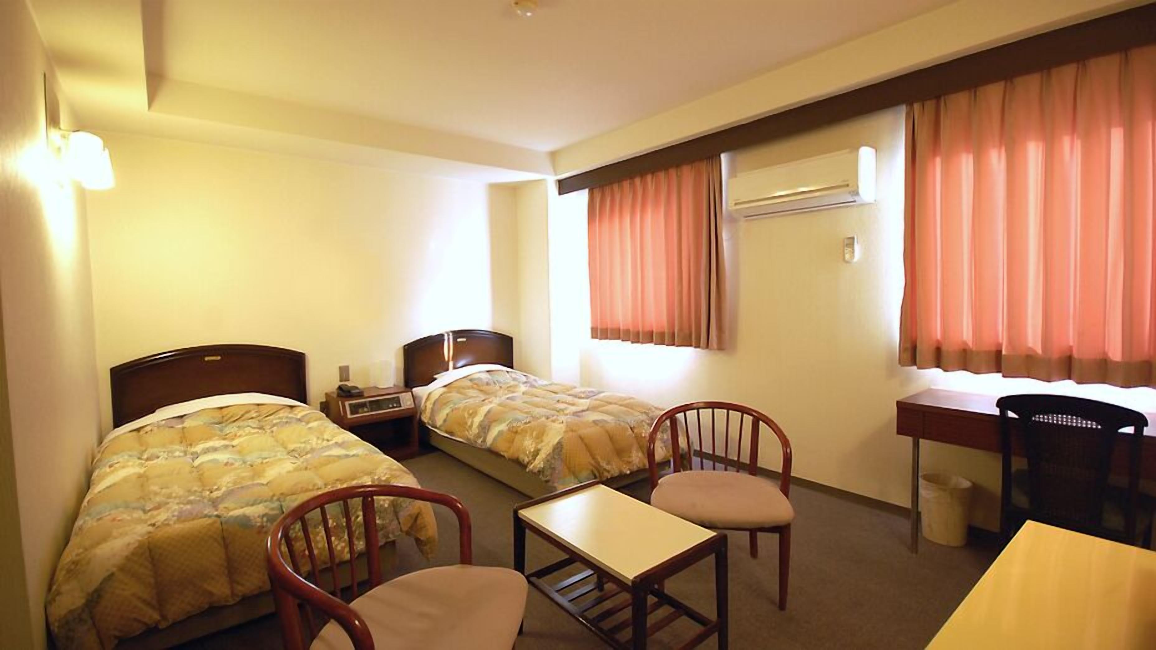 Ein Hotelzimmer mit zwei Betten, einem Schreibtisch, einem Stuhl und einer Klimaanlage.