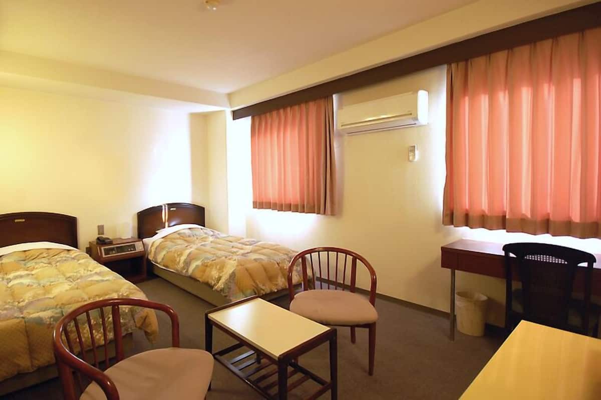 Una habitación de hotel con dos camas, un escritorio, una silla y un equipo de aire acondicionado.