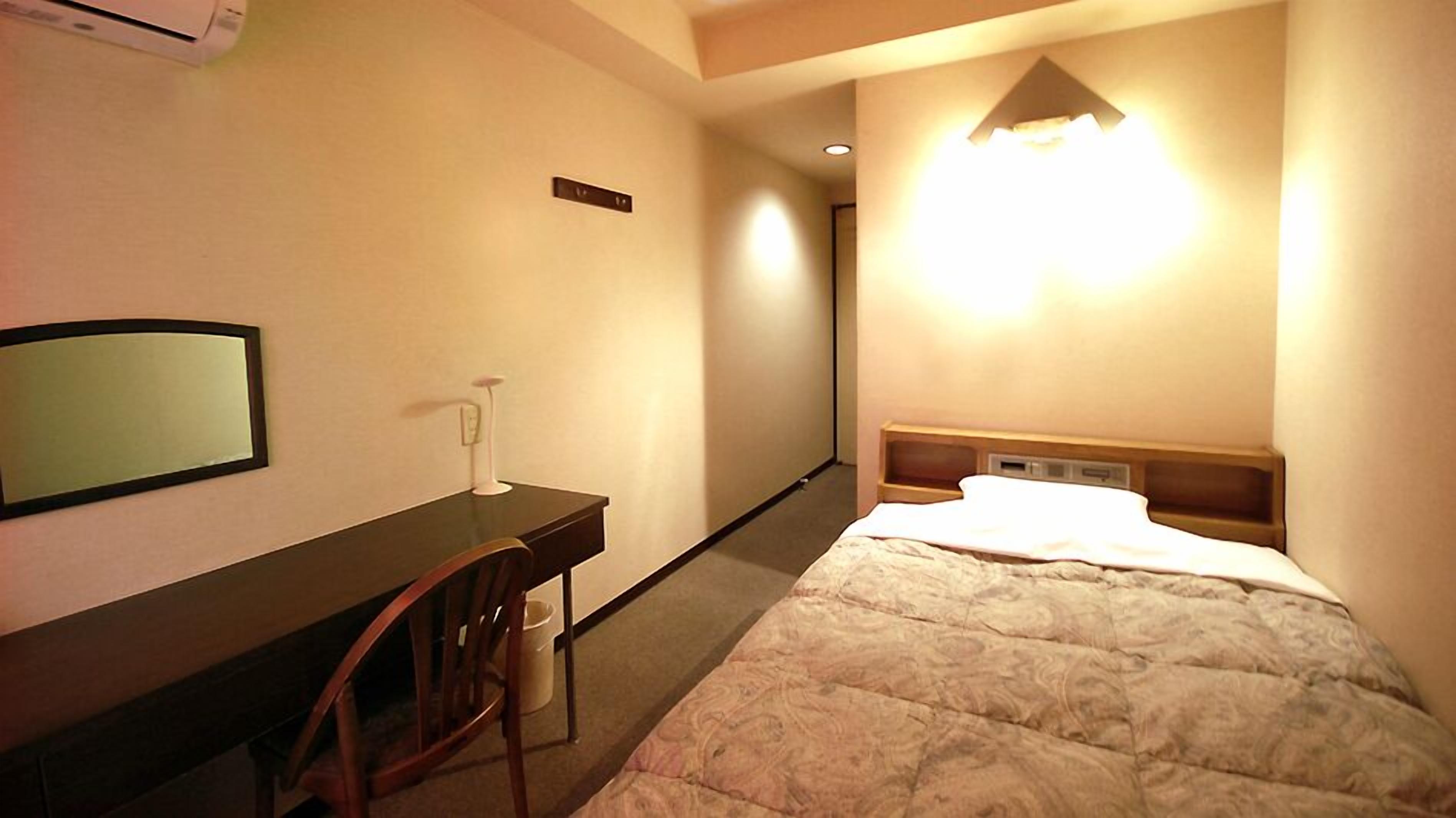Ein Hotelzimmer mit einem Bett, einem Schreibtisch, einem Sessel, einem Spiegel und einer Wandleuchte.