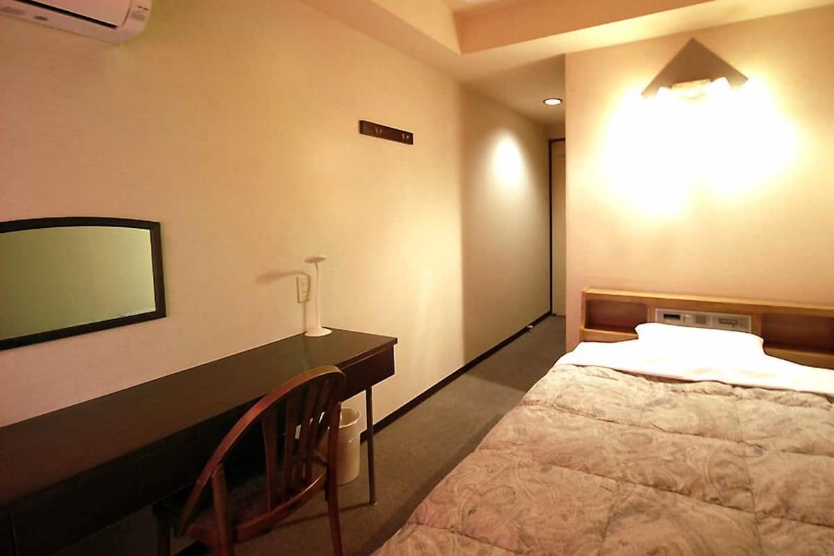 Habitación de hotel con cama, escritorio, silla, espejo y una lámpara fijada a la pared.