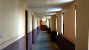 Un long couloir étroit, typique des hôtels, avec des portes des deux côtés, un sol recouvert de moquette et un tapis bleu courant au milieu.