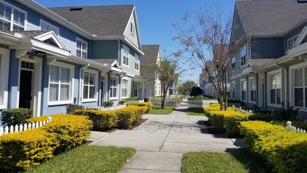 Fileira de casas geminadas com um caminho central, cercas brancas de piquete e jardins bem cuidados.