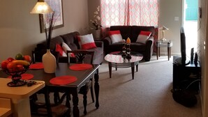 Uma sala de estar com área de jantar, ventilador de teto e janela com cortinas estampadas.