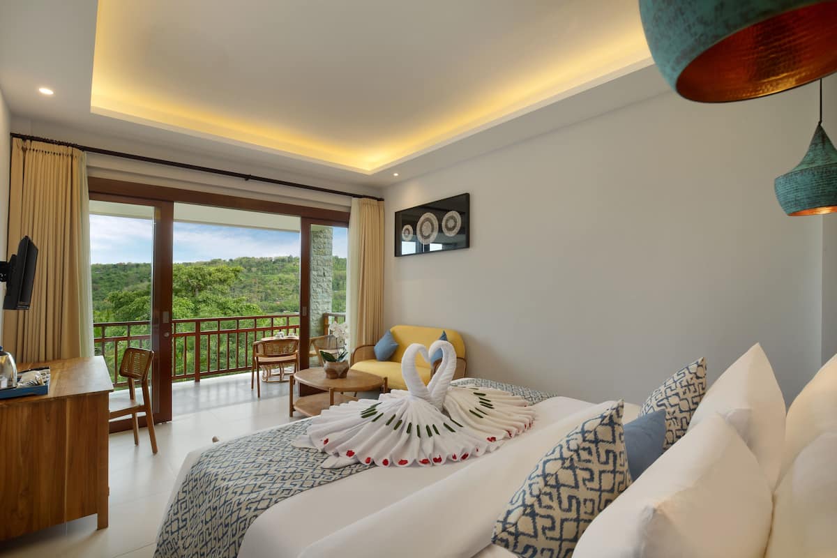 Une chambre d’hôtel avec un grand lit, un bureau, une chaise et un balcon donnant sur un paysage verdoyant.