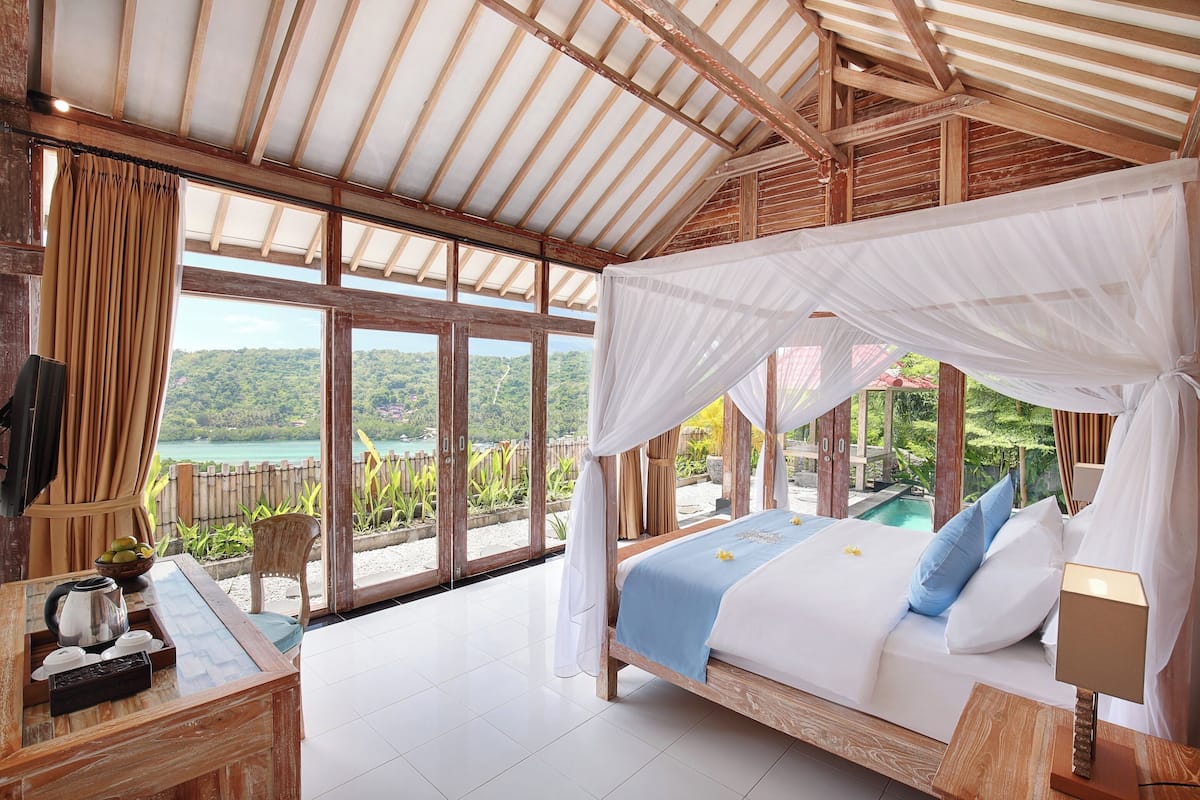 Une chambre à coucher avec un lit, une table de chevet, une fenêtre avec des rideaux et une vue sur un paysage naturel.