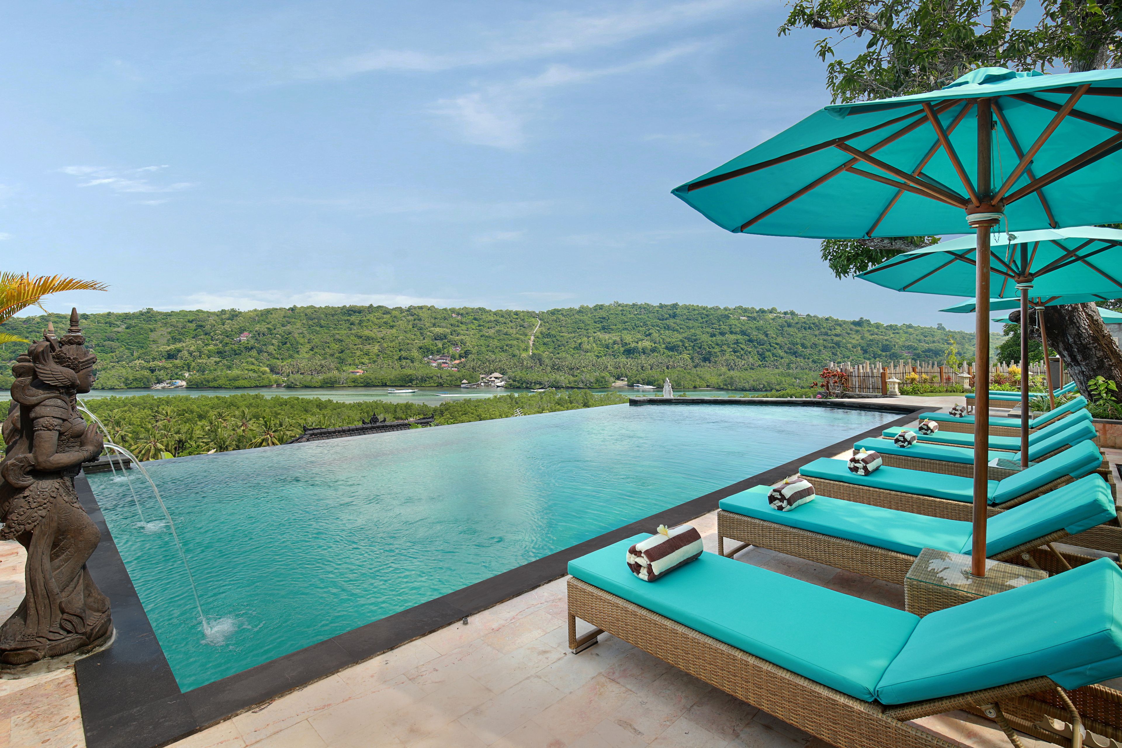 Une piscine entourée de verdure, dotée de chaises longues et de parasols, et offrant une vue sur un paysage lointain.