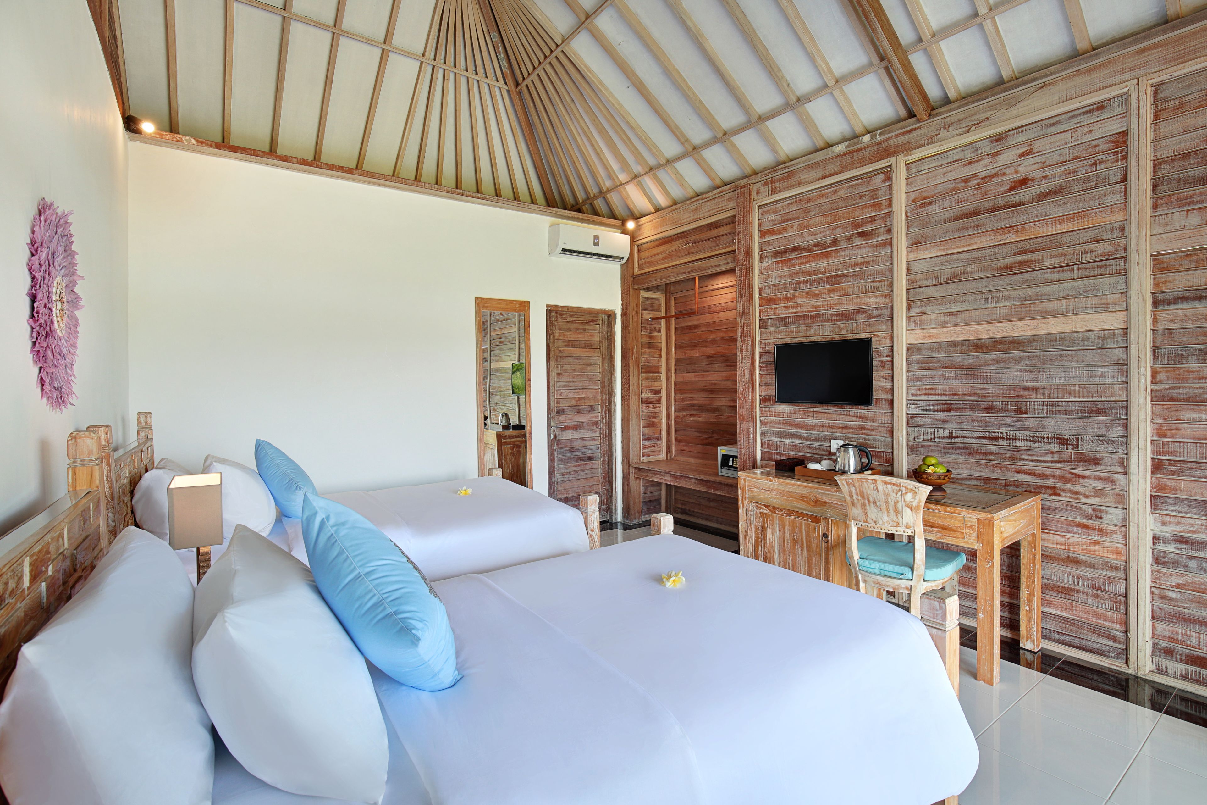 A room with two beds, a wooden desk, a television, and a wall-mounted air conditioning unit.