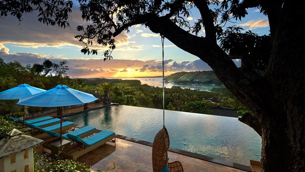 A pool area with lounge chairs and umbrellas, overlooking a scenic landscape with a sunset. - The Acala Shri Sedana (Lembongan Island)
