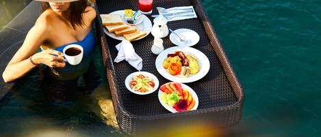 Bandeja de mimbre con alimentos para el desayuno, como tostadas, huevos y fruta, colocada junto a una piscina.