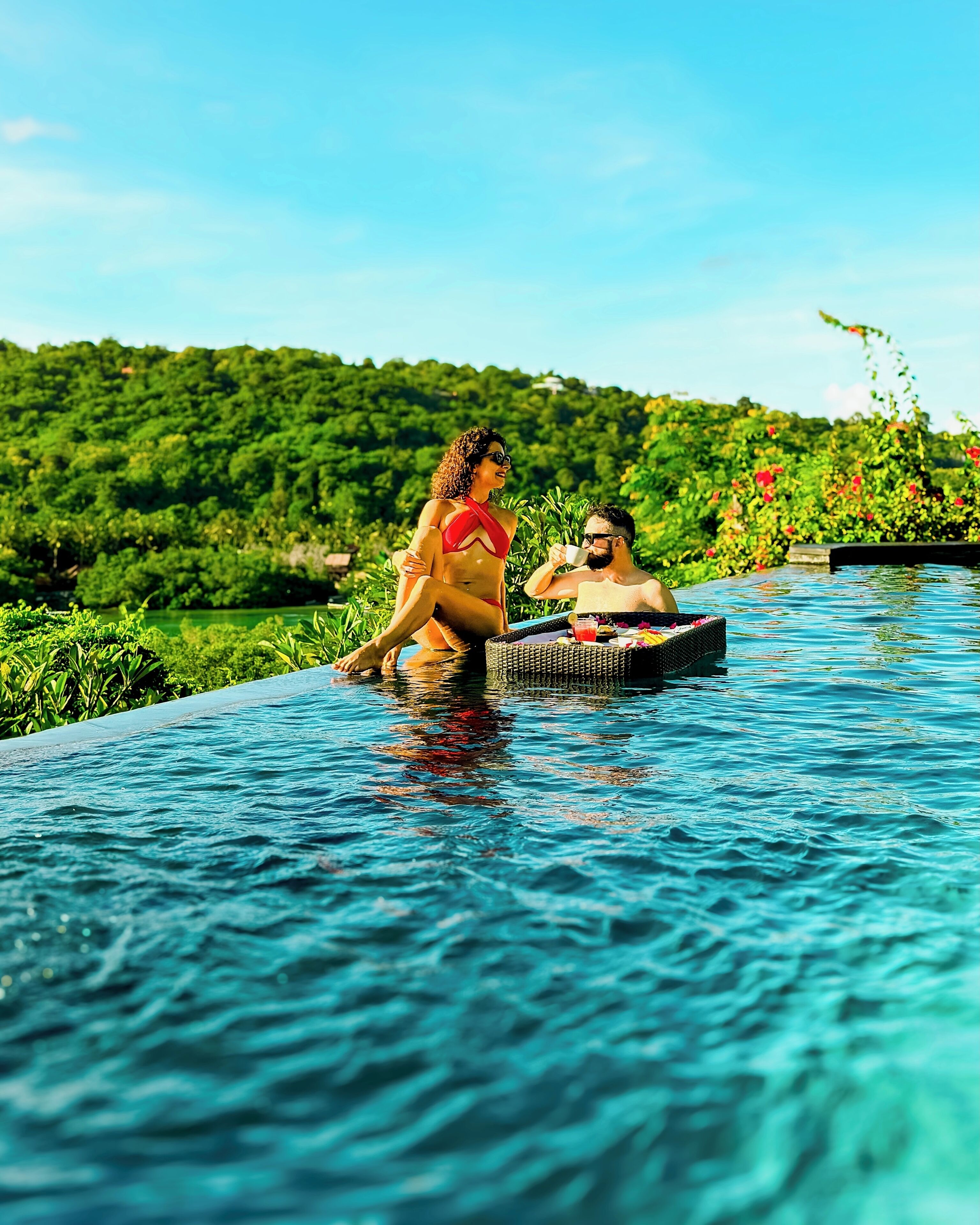 A couple in a swimming pool with a lush green landscape in the background.