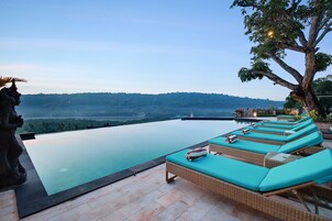 An infinity pool with lounge chairs and a statue, overlooking a scenic landscape.